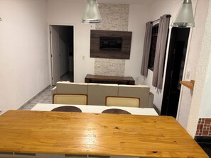 A dining area with a wooden table, cushioned chairs, a sofa, and a wall-mounted TV. - 2 suites with air conditioning, a hot tub, and a barbecue area (São José dos Campos)