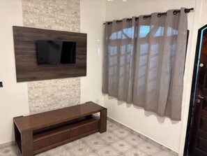 Ein Zimmer mit an der Ziegelwand befestigtem Fernseher, einer Holzeinrichtungsanlage, gemusterten Bodenfliesen und einer Tür mit Vorhang.