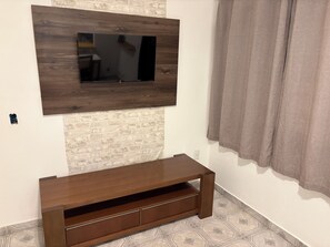 A room with a mounted TV, a wooden entertainment unit, a brick-patterned wall, and a patterned floor.