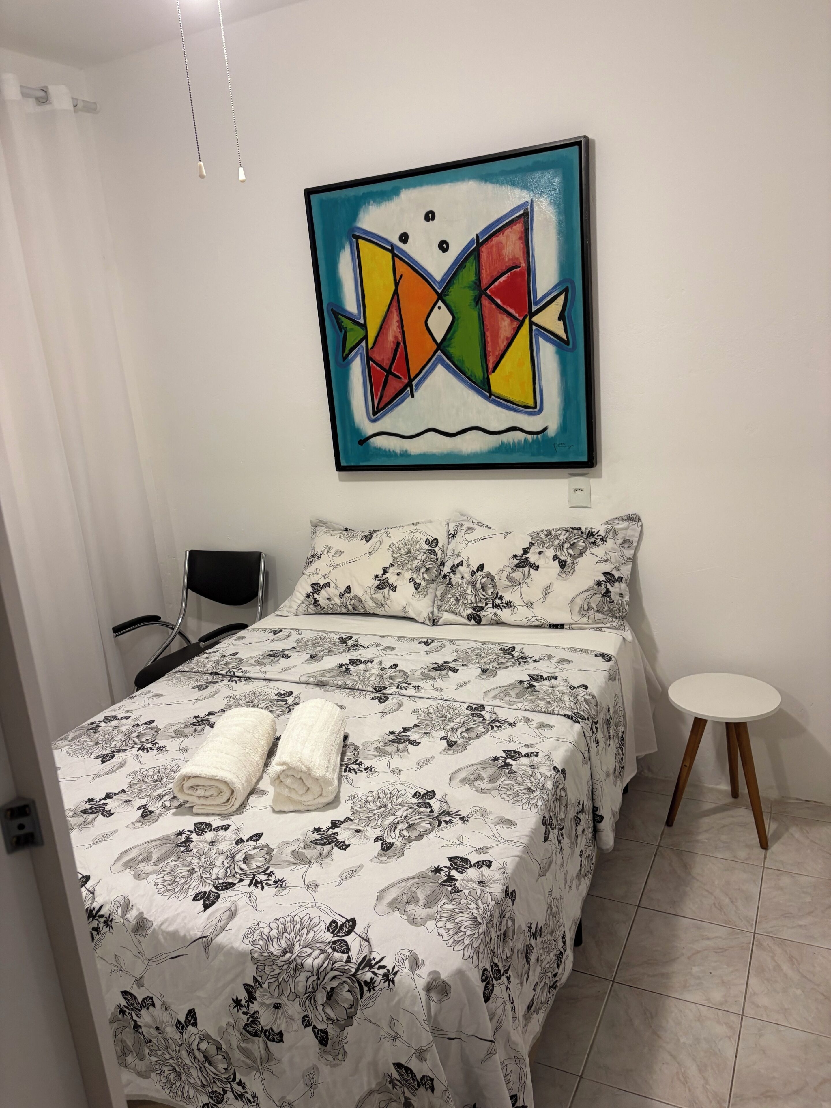 A bedroom with a bed, floral bedding, a small round table, and a colorful abstract painting on the wall.