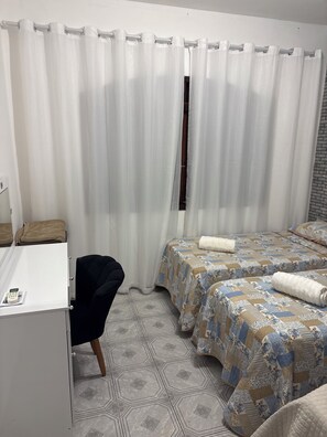 Une chambre d’hôtel avec un bureau, deux lits avec une literie à motifs, une chaise et une fenêtre avec des rideaux.