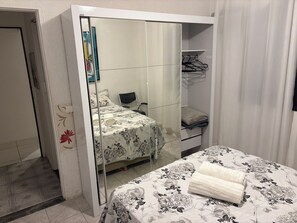 Ein Schlafzimmer mit einem Bett, einem Kleiderschrank, einem Sessel und einem Spiegel.