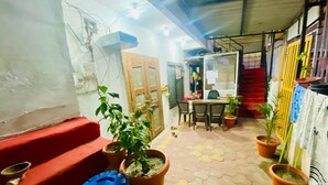 Un espace extérieur abrité, équipé d’une table et de chaises, de plantes en pot et d’un banc rouge.