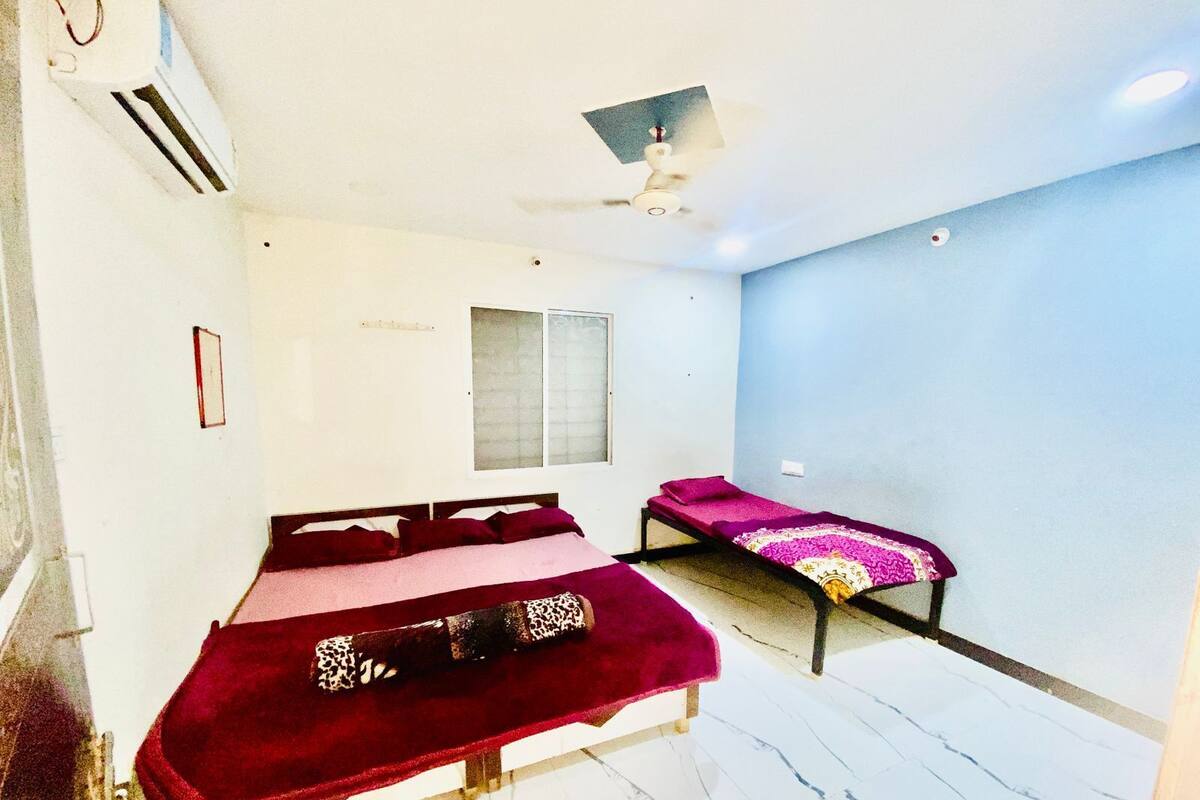 A room with two beds, a ceiling fan, a window, and an air conditioning unit.