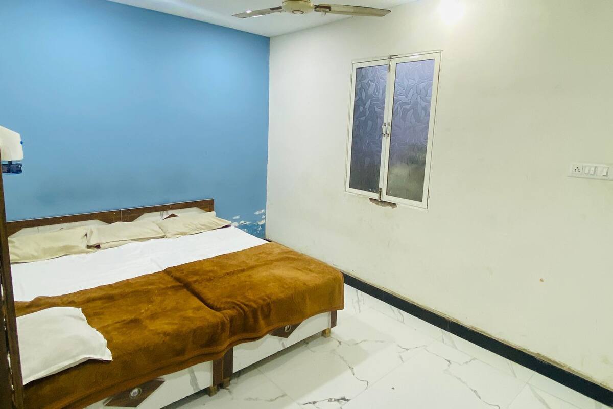 A bedroom with a bed, a ceiling fan, a window, and a wall socket.