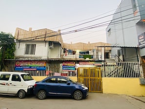 A building with multiple signs, including one for a hotel and another for a laundry service. There are two cars parked in front. - Shree Niwas Yatri Grah (Ujjain)
