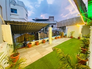 A rooftop garden with potted plants, a small lawn, and a metal roof structure. - Shree Niwas Yatri Grah (Ujjain)