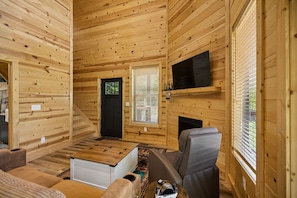 Ein Holzblockhaus-Innenraum mit einer Couch, einem an der Wand montierten Fernseher und einem Kamin.