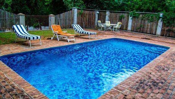 A rectangular swimming pool with a brick border, surrounded by lounge chairs and a table. - The White House  (Victoria Falls)