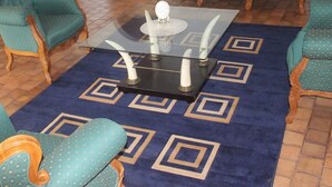 A room with a green sofa, a matching armchair, a glass coffee table, and a patterned rug. - The White House  (Victoria Falls)