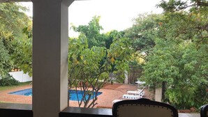 A view of a swimming pool surrounded by lush greenery, with a patio area and lounge chairs visible. - The White House  (Victoria Falls)