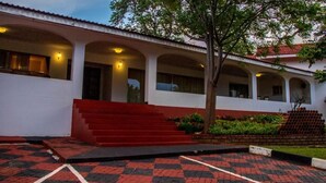 Un edificio con una escalera roja que conduce a un vestíbulo cubierto, un camino de entrada empavedado y un árbol en primer plano.
