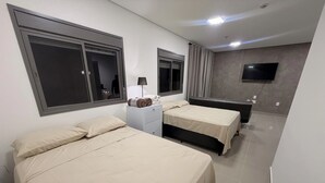 A hotel room with two beds, a desk, a lamp, a TV, and a window with curtains. - Modern Studio in the Best Area of ​​Mooca (São Paulo)