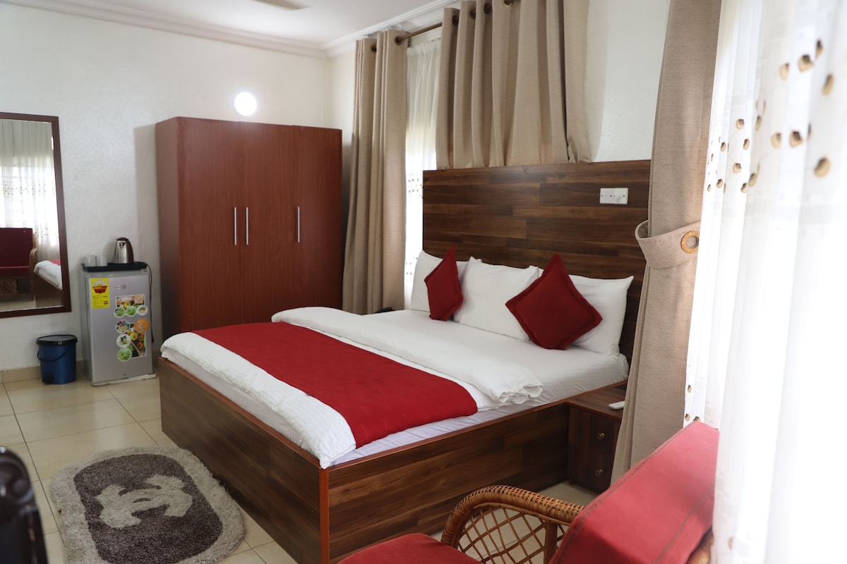 Camera d'albergo con un letto in legno, cuscini rossi, un armadio, un tavolino e un cestino.