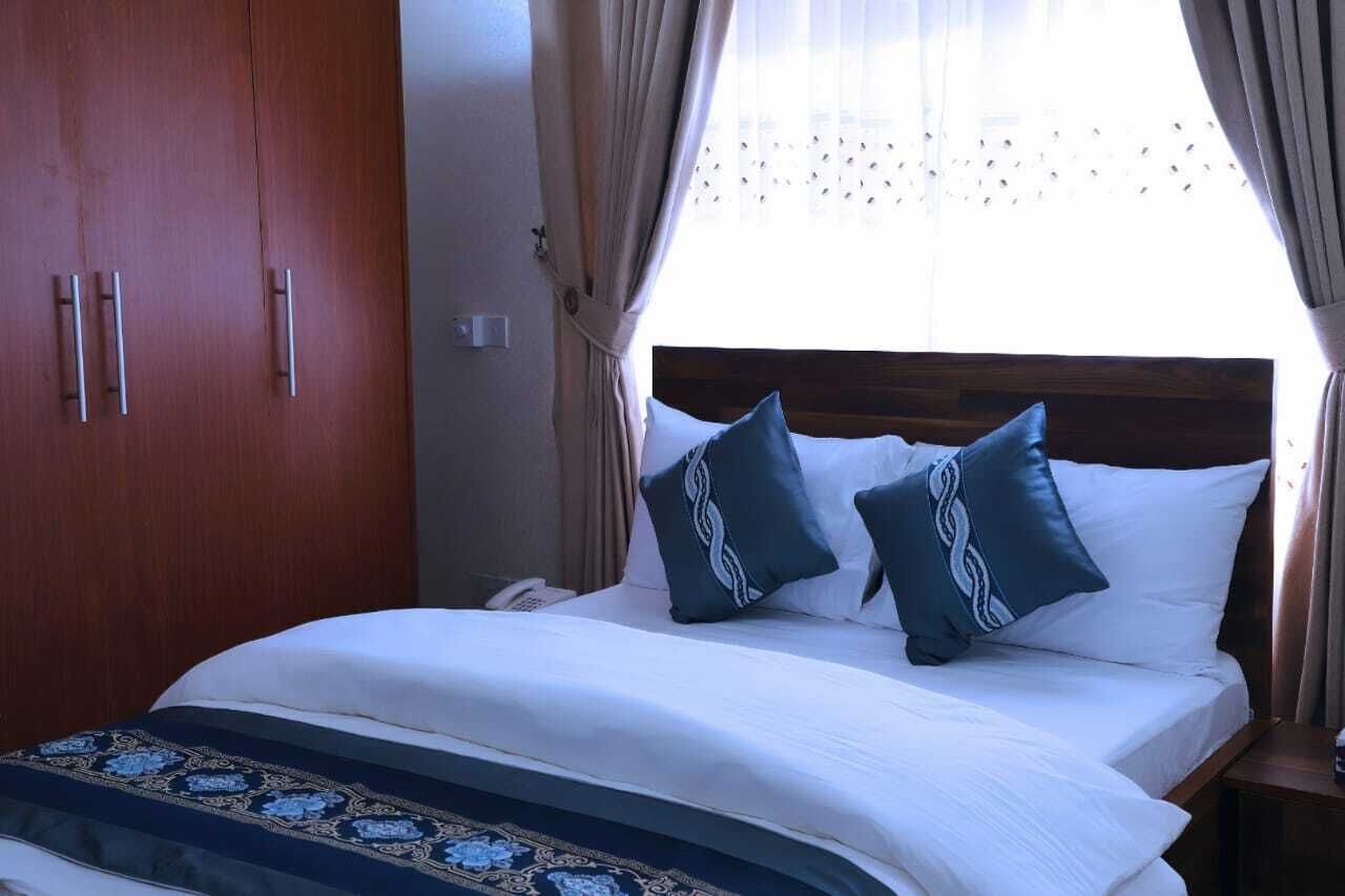 A hotel room with a bed, a wooden wardrobe, and a window with curtains.
