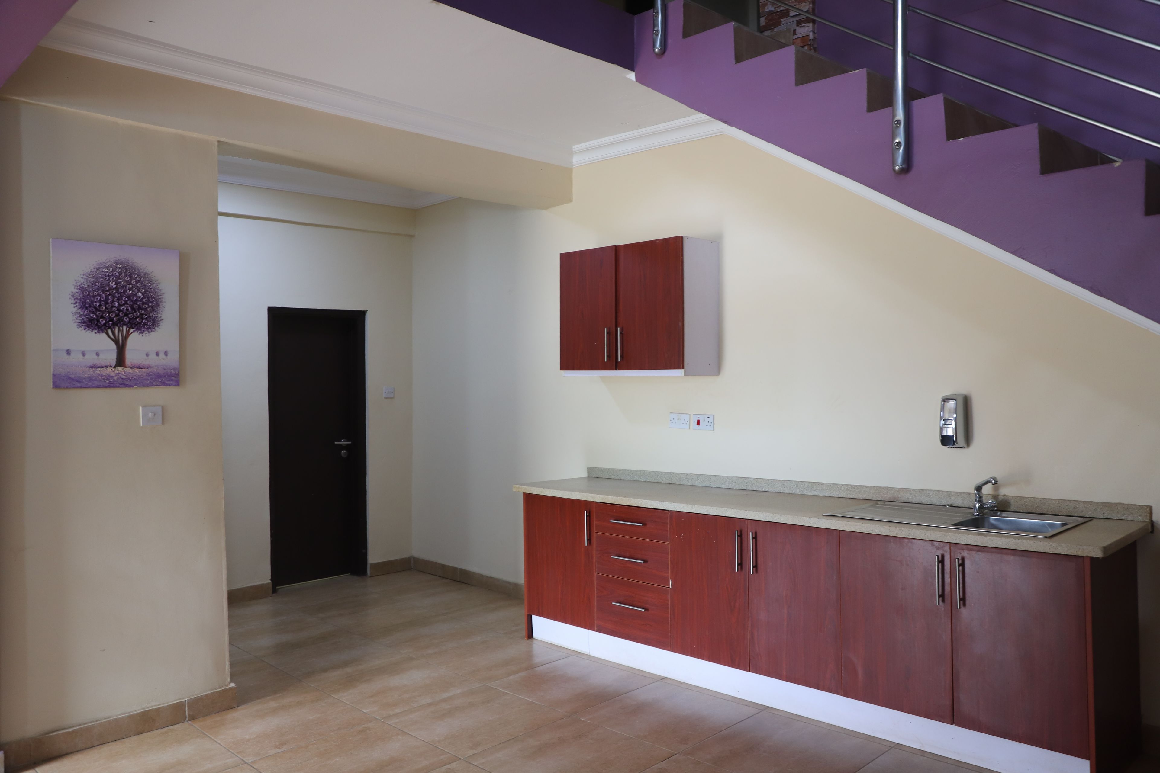 A kitchen with a built-in sink, wooden cabinets, and a staircase leading to an upper level.
