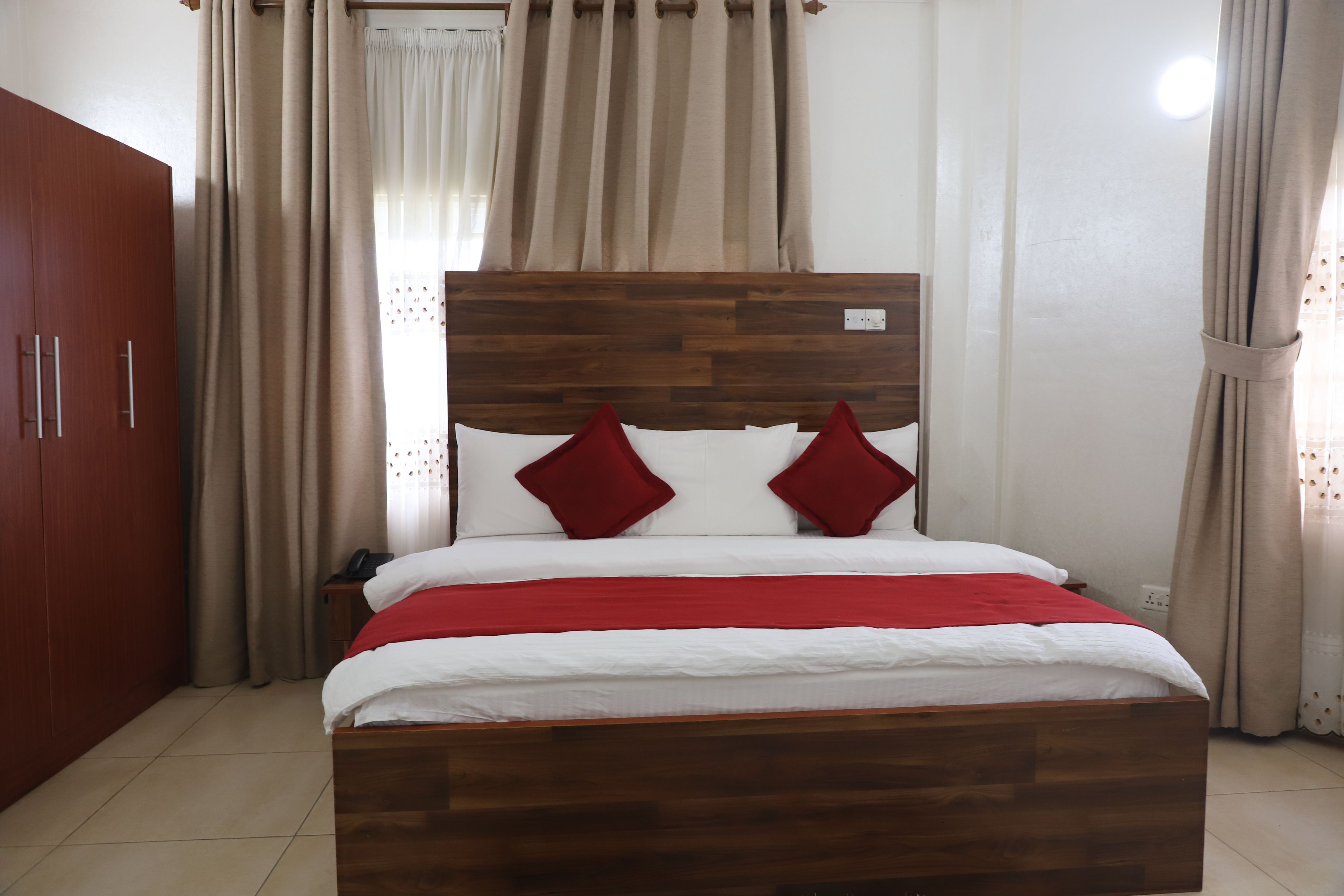 Un dormitorio con cabecera de madera, cama con ropa de cama blanca y roja, y un armario.