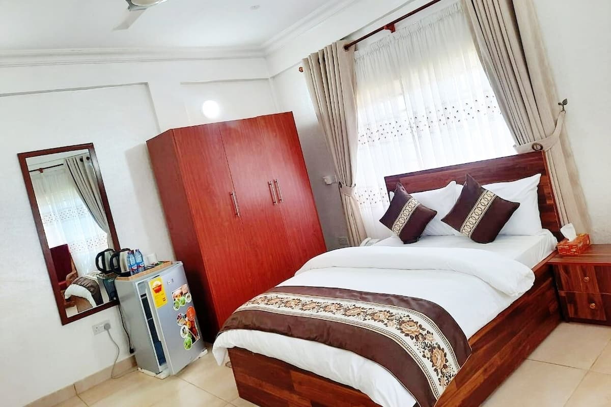 Une chambre à coucher comprenant un lit, une armoire, un miroir, un ventilateur de plafond et une fenêtre avec des rideaux.