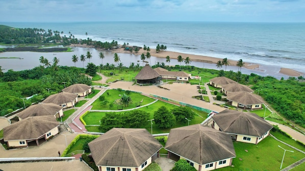 Un resort con varias construcciones tipo bungalow, un espacio común central y vista al mar.
