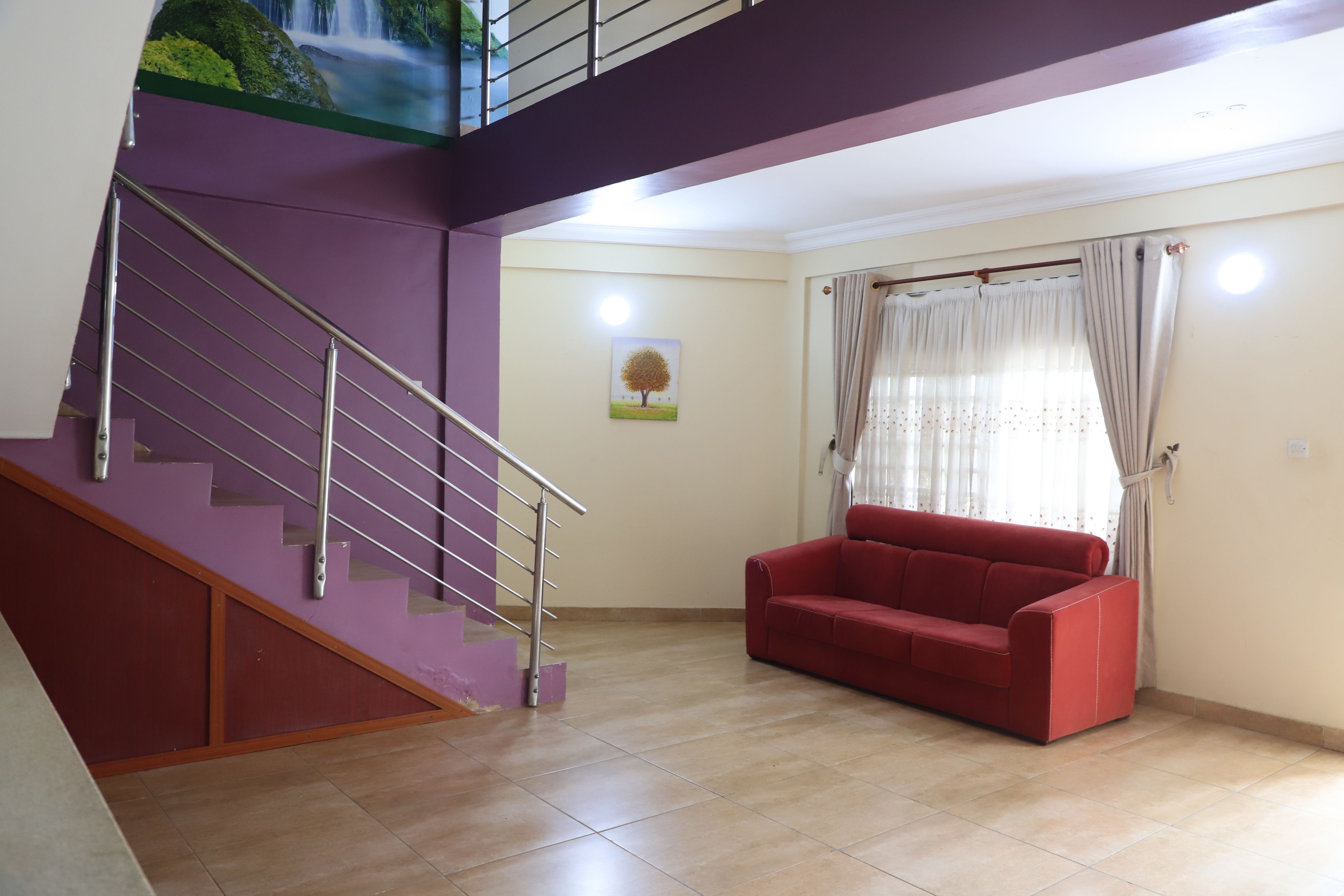Una sala de estar con una escalera, un sofá rojo y un cuadro en la pared.