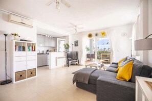 Eine moderne Wohnung mit Wohnzimmer, Küche und Essbereich, ausgestattet mit einem grauen Sofa, einem Fernseher und einem Balkon mit Blick.