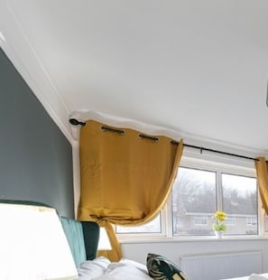 Ein Schlafzimmer mit einem Bett, einem Fenster mit Vorhängen, einer Heizung und einer Pflanze auf der Fensterbank.