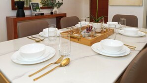 Een eettafel gedekt met witte borden, kommen, glazen en gouden bestek.