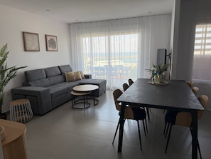 Una sala de estar moderna con un sofá gris, una mesa de centro redonda y una zona de comedor con una mesa y sillas oscuras.