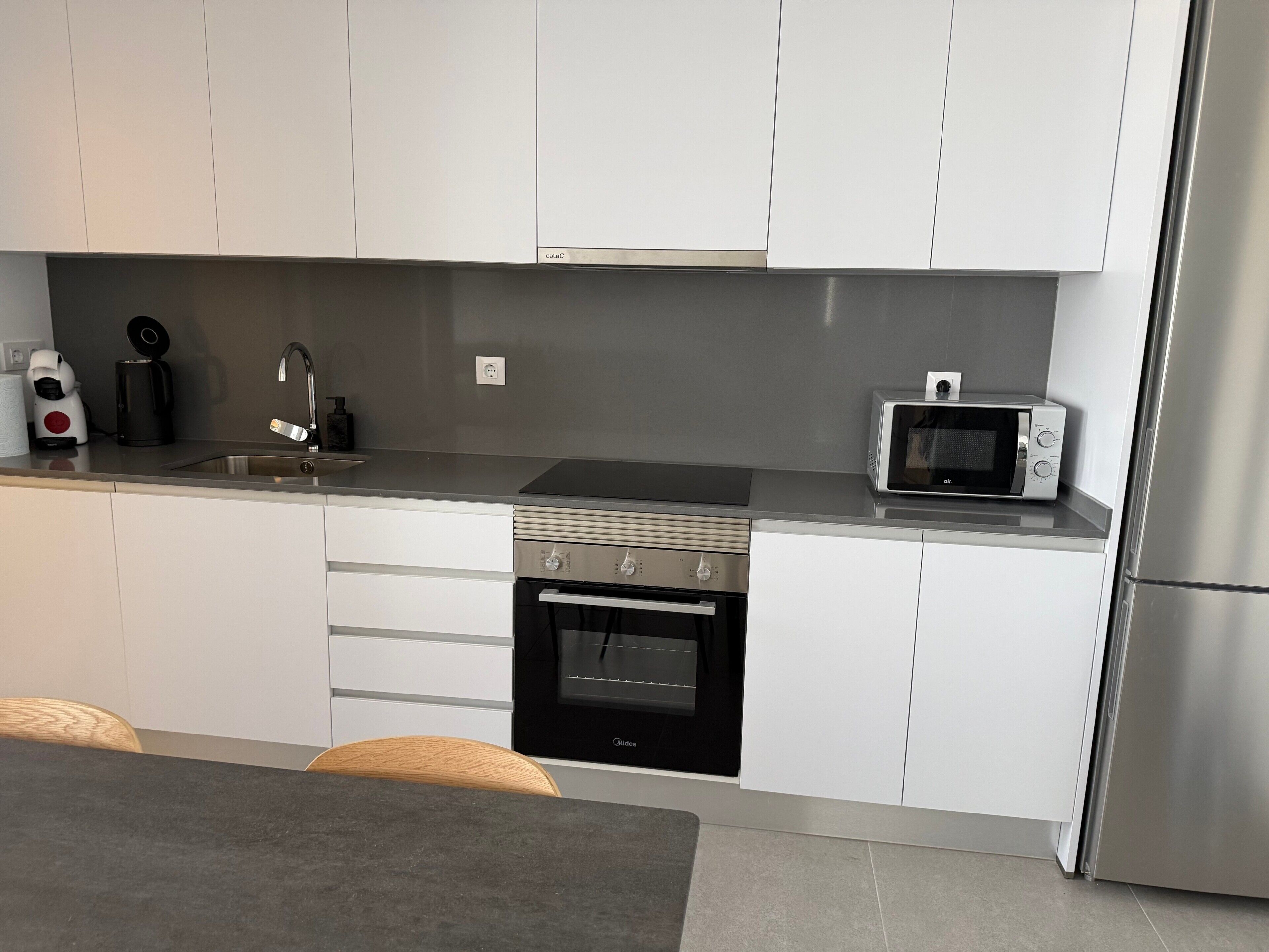 A modern kitchen with white cabinets, a stainless steel refrigerator, a microwave, a coffee maker, and a built-in oven.