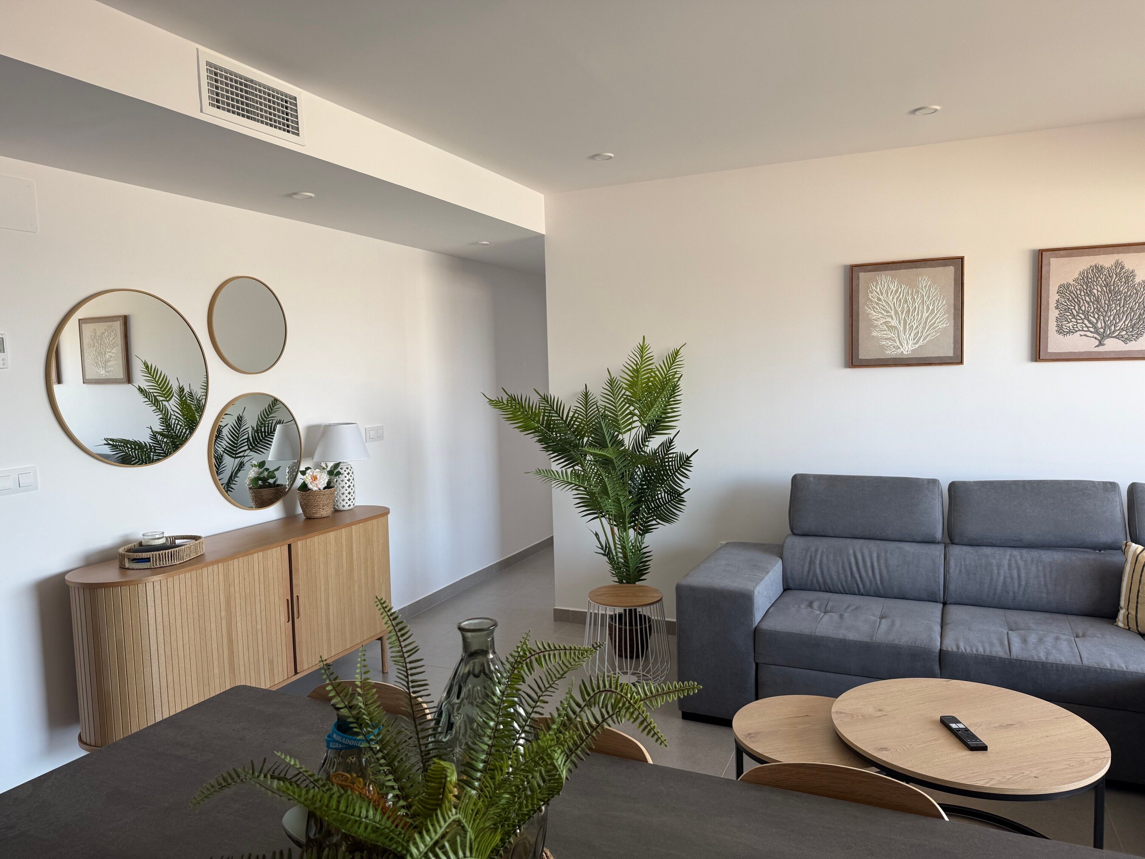 Ein modernes Wohnzimmer mit einem grauen Sofa, runden Spiegeln und einem Essbereich mit Tisch und Stühlen.