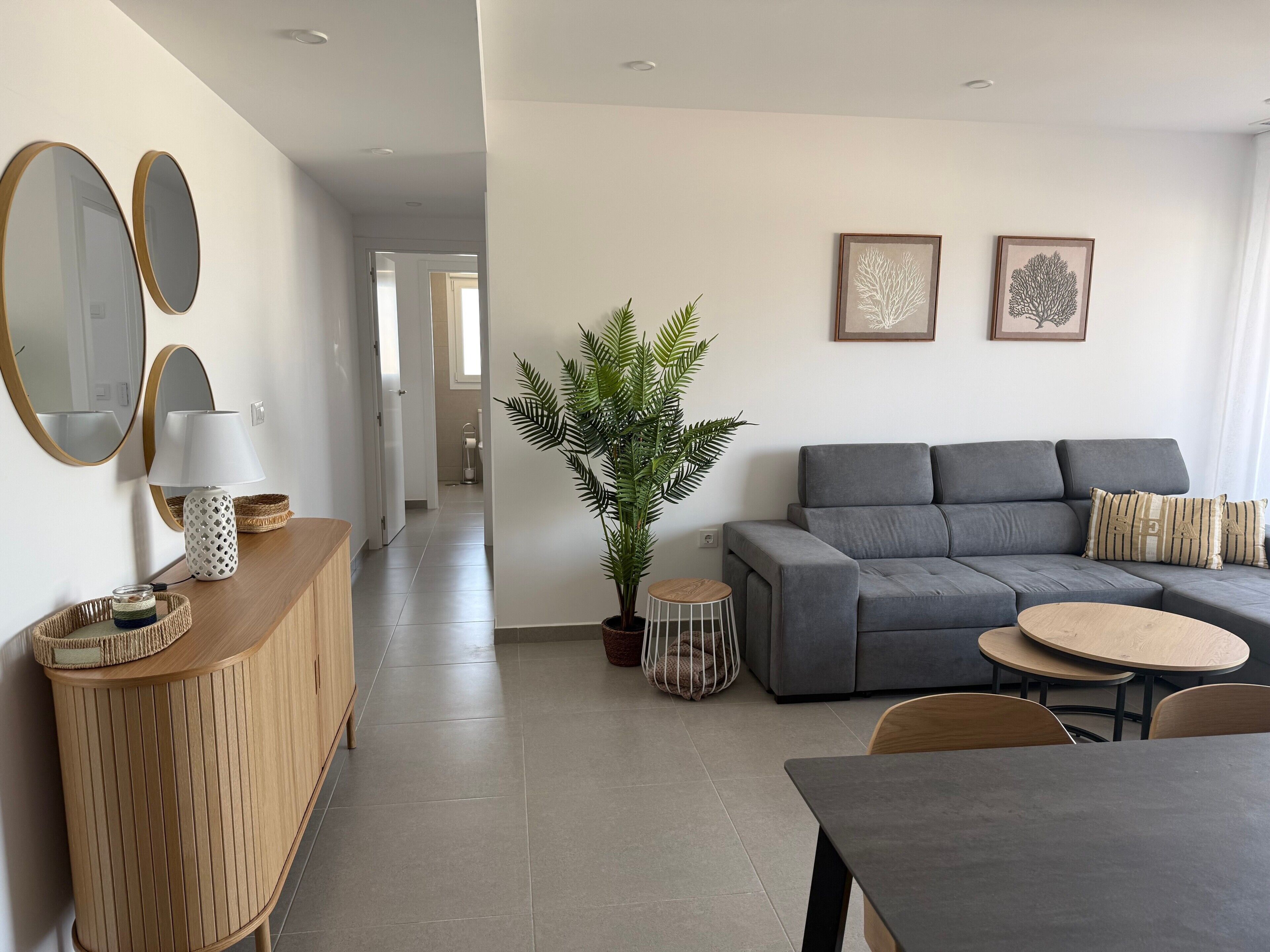 Ein modernes Wohnzimmer mit einem grauen Sofa, einem Esstisch und einer Topfpflanze.
