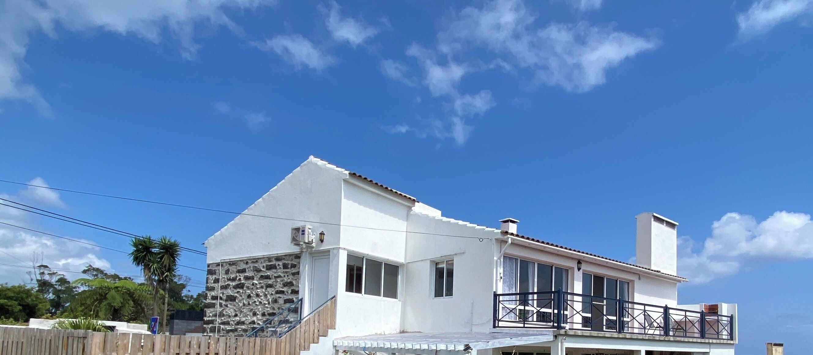 A white building with a stone facade, a balcony with a metal railing, and a clear blue sky.