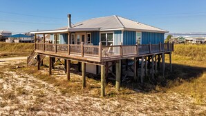 A coastal house with a deck, situated on stilts in a grassy area. - Sea Glass, Gulf Beachside, 3/2, Sleeps 9 (Dauphin Island)