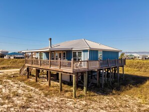 A coastal house with a deck, situated on stilts in a grassy area. - Sea Glass, Gulf Beachside, 3/2, Sleeps 9 (Dauphin Island)