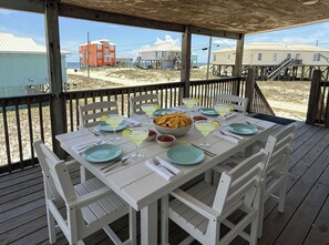A covered outdoor dining area with a table set for two, overlooking a beach with buildings in the background.