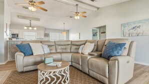 A modern living room with a sectional sofa, two ceiling fans, a round coffee table, and a kitchen in the background. - Sea Glass, Gulf Beachside, 3/2, Sleeps 9 (Dauphin Island)