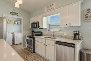 A modern kitchen with white cabinetry, a stainless steel dishwasher, a built-in microwave, and a coffee maker. - Sea Glass, Gulf Beachside, 3/2, Sleeps 9 (Dauphin Island)