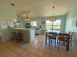 A kitchen with a central island, bar stools, a dining table with chairs, and a view through the window. - Sea Glass, Gulf Beachside, 3/2, Sleeps 9 (Dauphin Island)