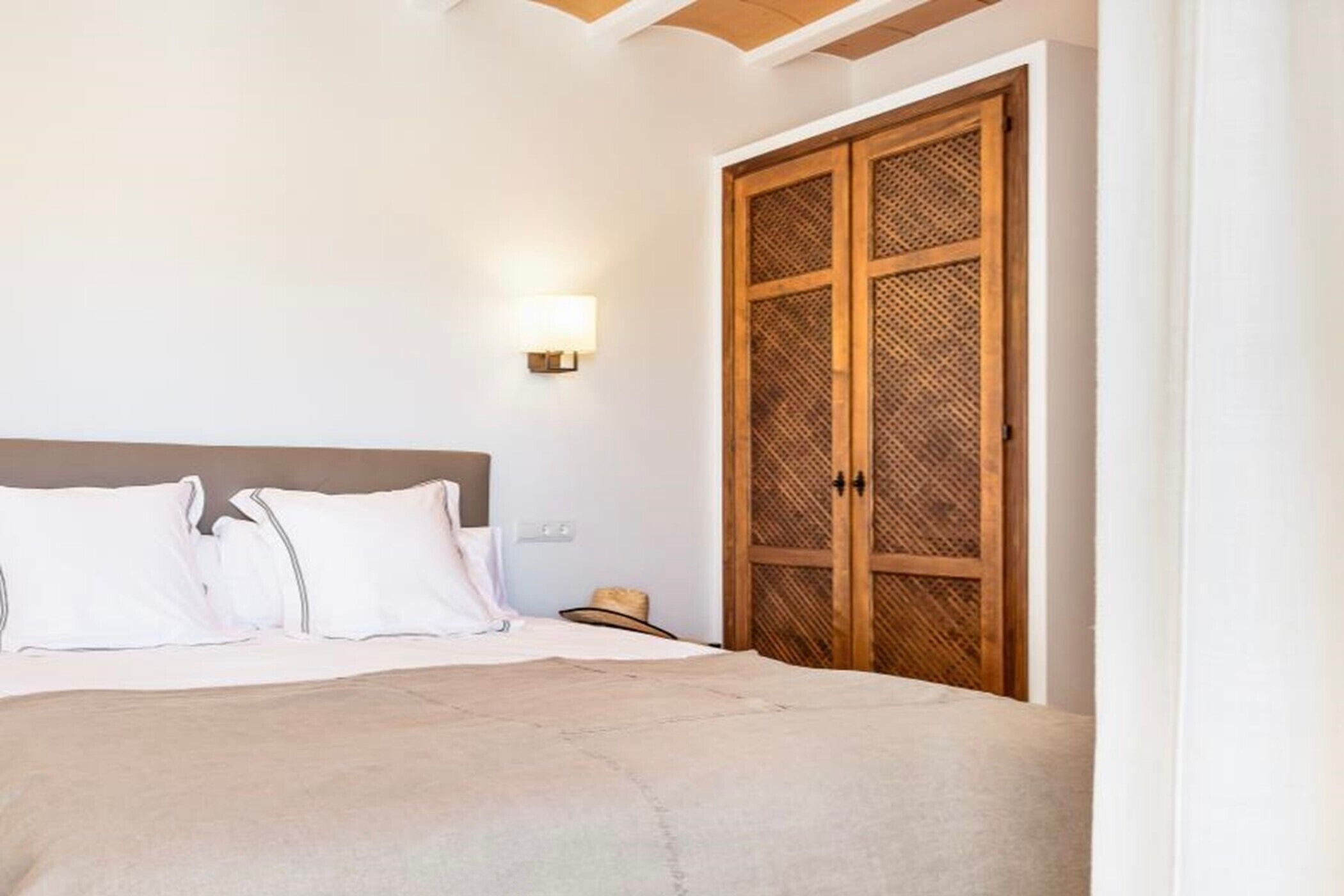 A bedroom with a bed, white pillows, a wooden wardrobe, and a wall-mounted light.
