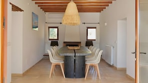 A dining area with a central table, chairs, a hanging light fixture, and a fireplace.