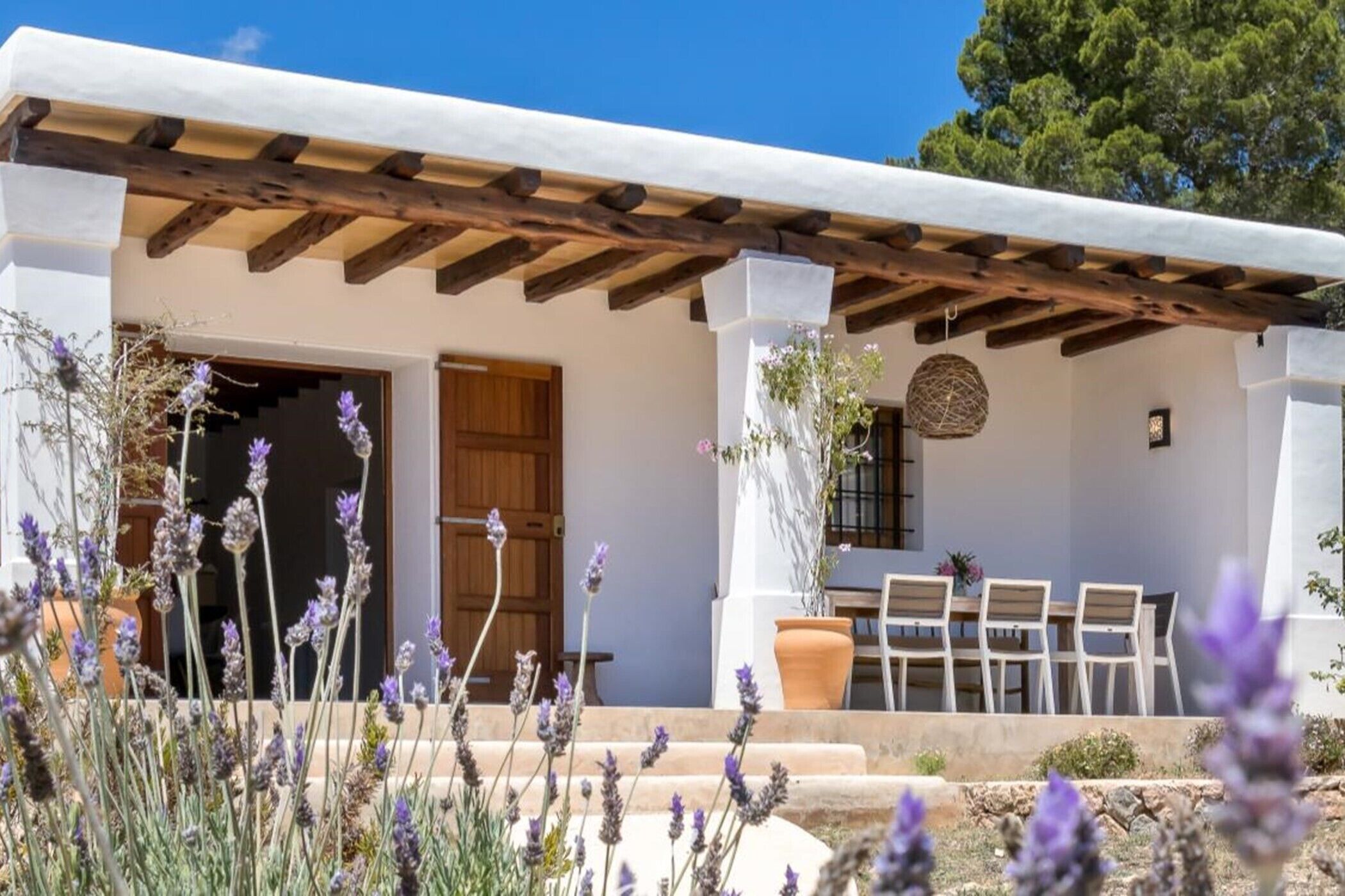 Un edificio con una pérgola, una puerta de madera y un patio con sillas y una mesa.