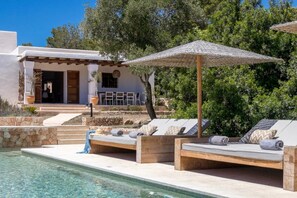 A poolside area with wooden loungers, a covered seating area, and a clear pool.