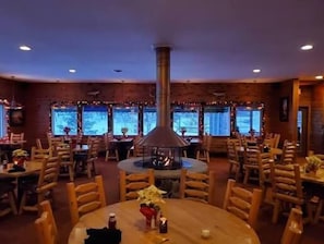 En restaurant med runde borde, træstole, en central skorsten og store vinduer.