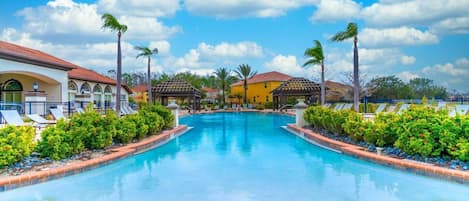 A swimming pool with lounge chairs, palm trees, and buildings in the background.