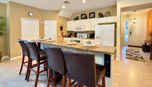 A kitchen with a central island, bar stools, white cabinets, a microwave, and a refrigerator. - Amazing Home Near Parks w/ Pool & Spa (Kissimmee)