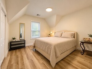 Une chambre à coucher avec un lit, une table de chevet, un miroir, une fenêtre et un luminaire au plafond.