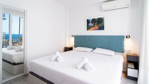 Een hotelkamer met een groot bed, twee nachtkastjes, een wandairconditioner en een schilderij boven het bed.