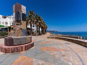 Eine Uferpromenade mit einem Steinmonument, Palmen und freiem Blick auf das Meer.