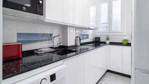 Een moderne keuken met witte kastjes, een zwarte magnetron en een raam met uitzicht.