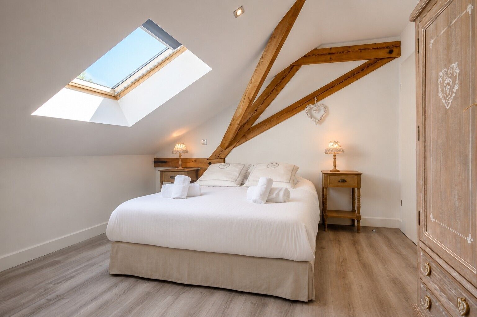 Een slaapkamer met dakraam, een bed met kussens, nachtkastjes met lampen en een houten kledingkast.